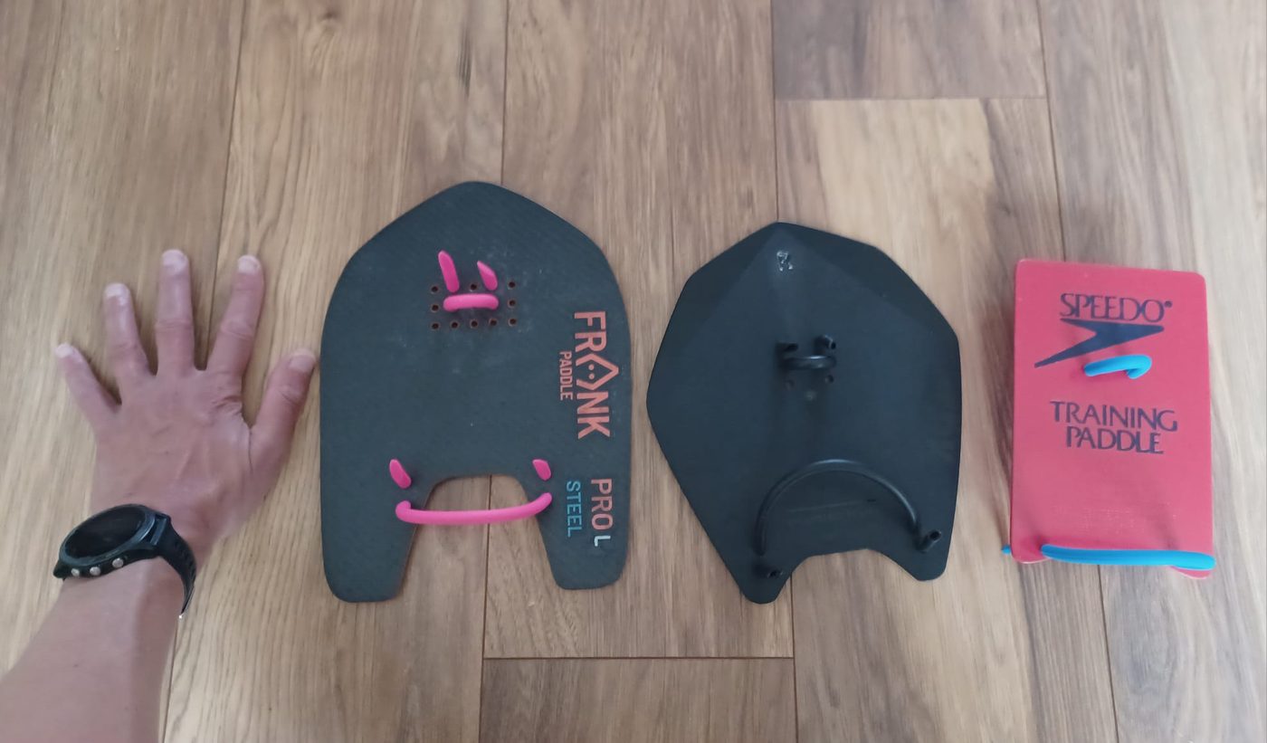 Frank Pro Steel Large carbon, ARK Blade Large plastic and old Speedo training paddles side by side with a hand for scale